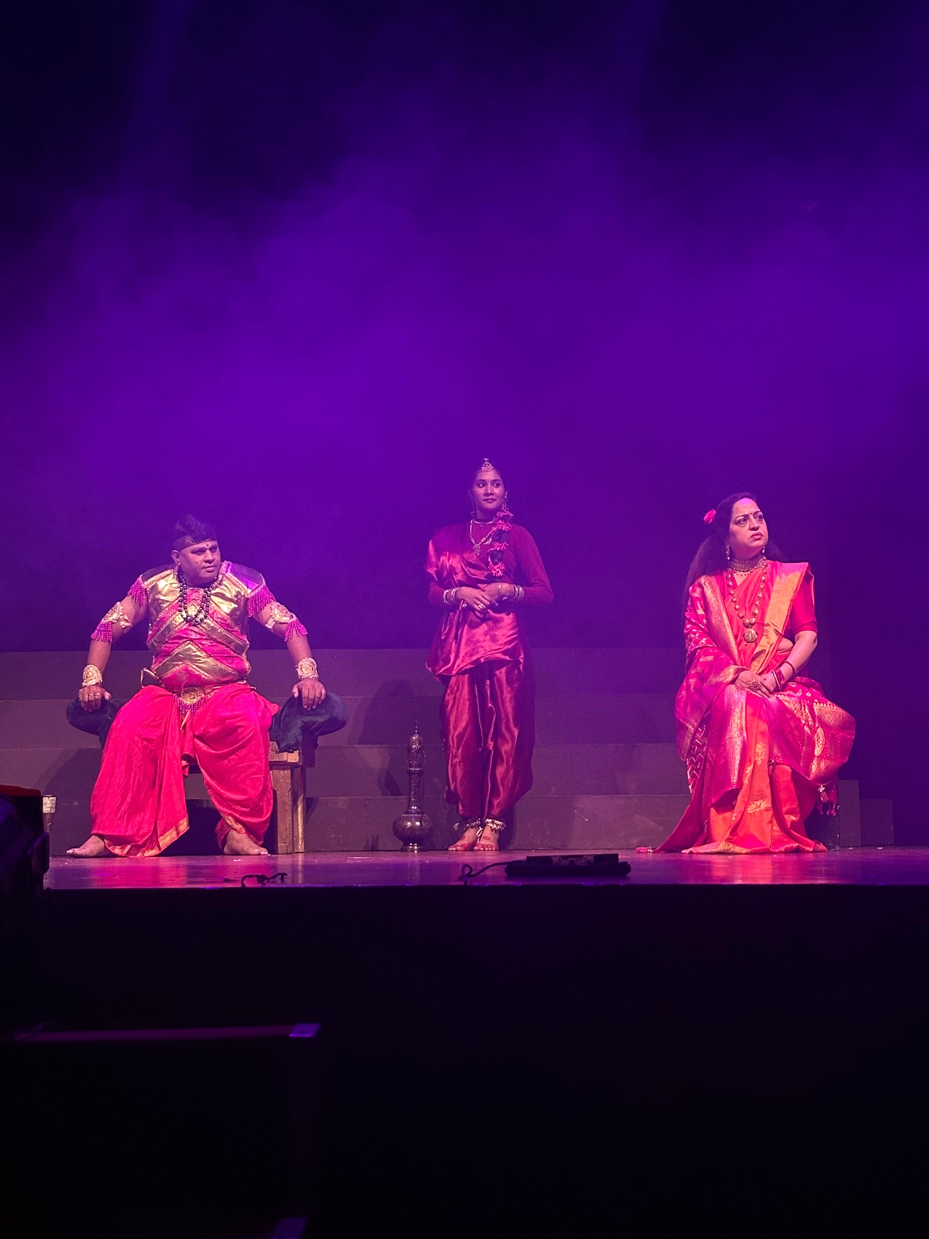 Three performers in a royal court scene under purple light