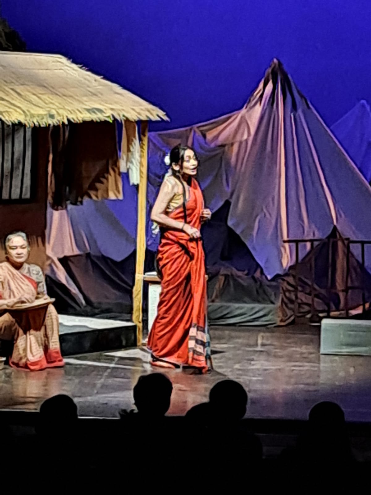 Actors performing beside a thatched hut set