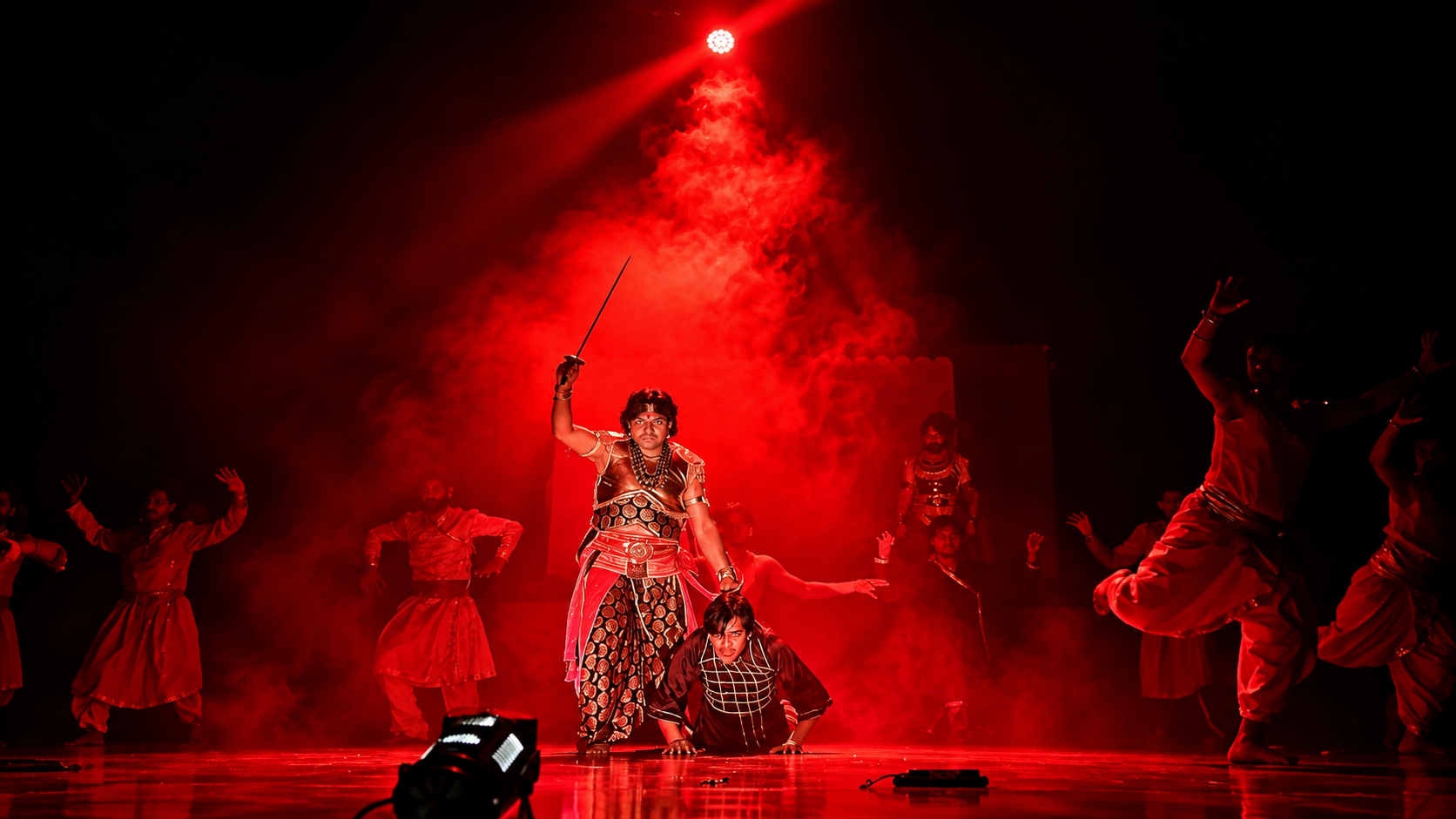 Dramatic ensemble scene with a raised sword under red lighting