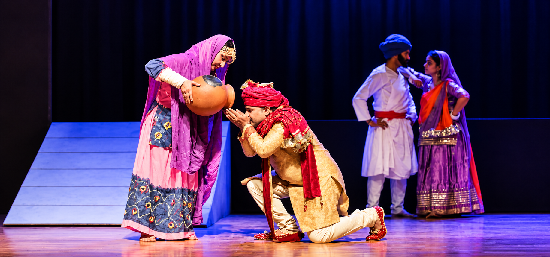 Costumed performers acting on stage under blue and purple lighting
